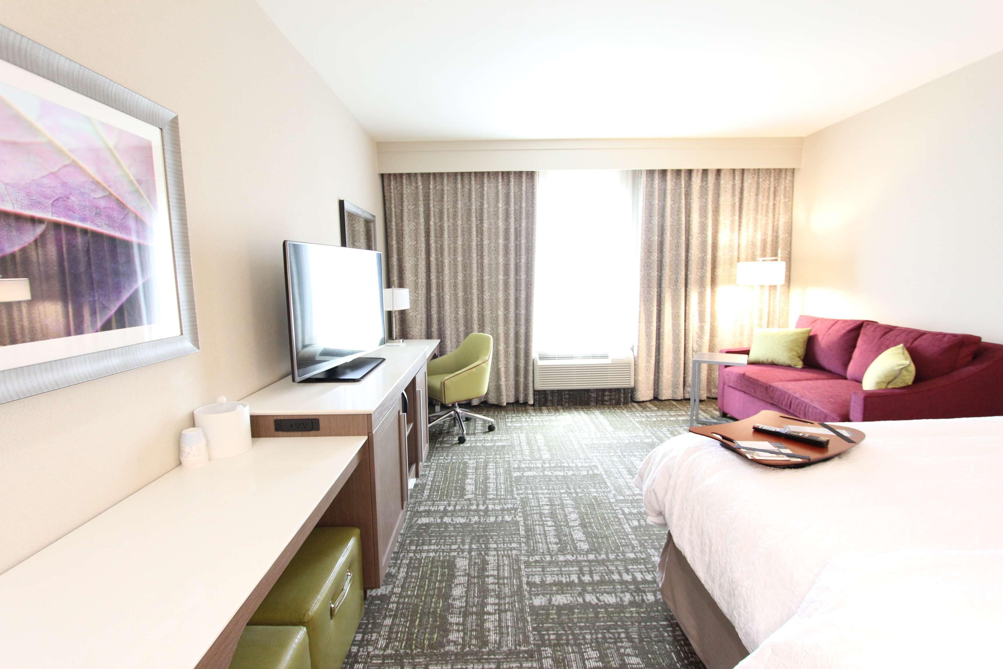 Una habitación de hotel con cama, escritorio con computadora, silla, sofá y televisor.