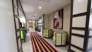 A hotel corridor with a patterned carpet, seating areas, and a reception desk. - Hampton Inn & Suites Dallas Market Center (Dallas)
