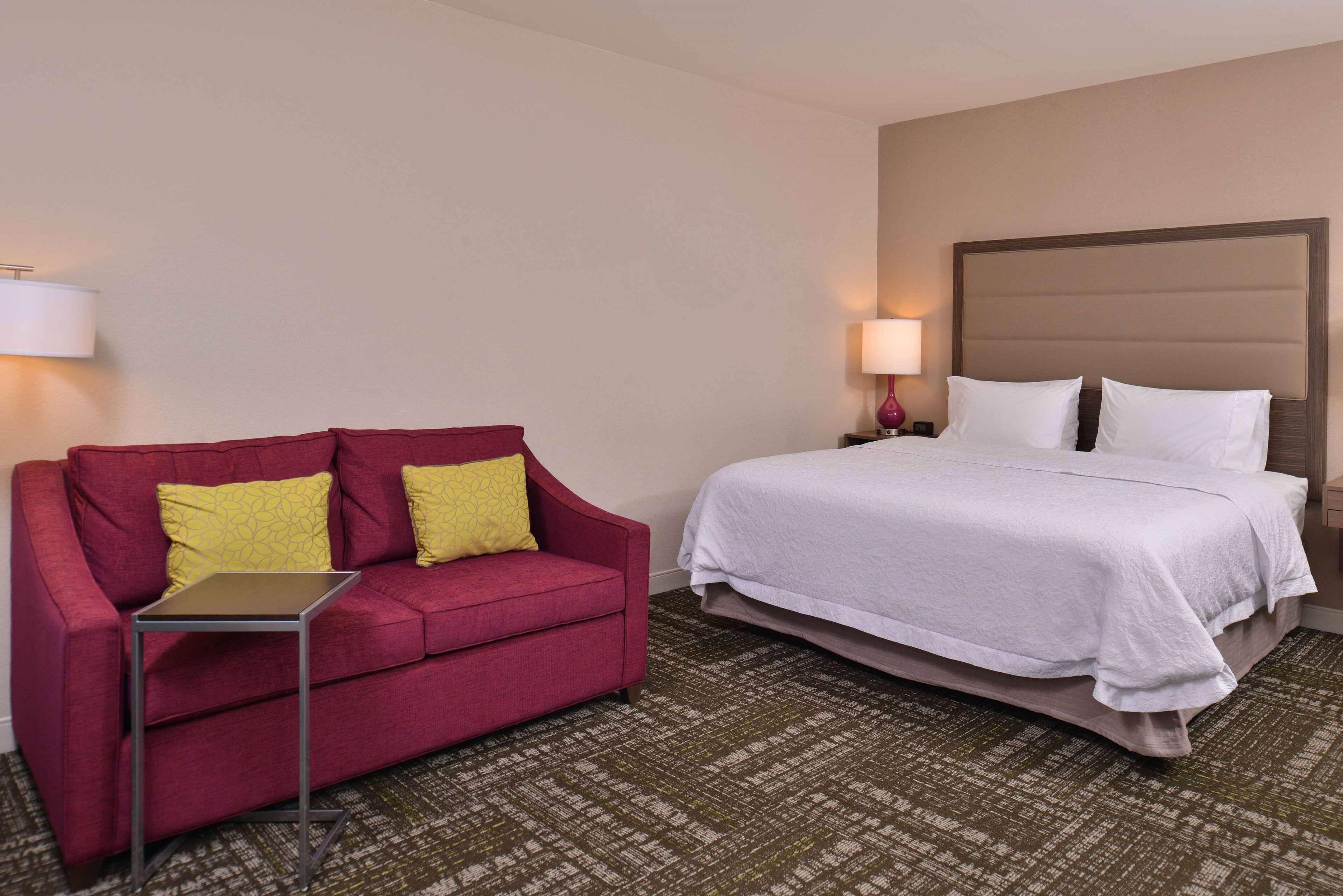 A hotel room with a red sofa, a small table, a bed with white bedding, and two bedside lamps.