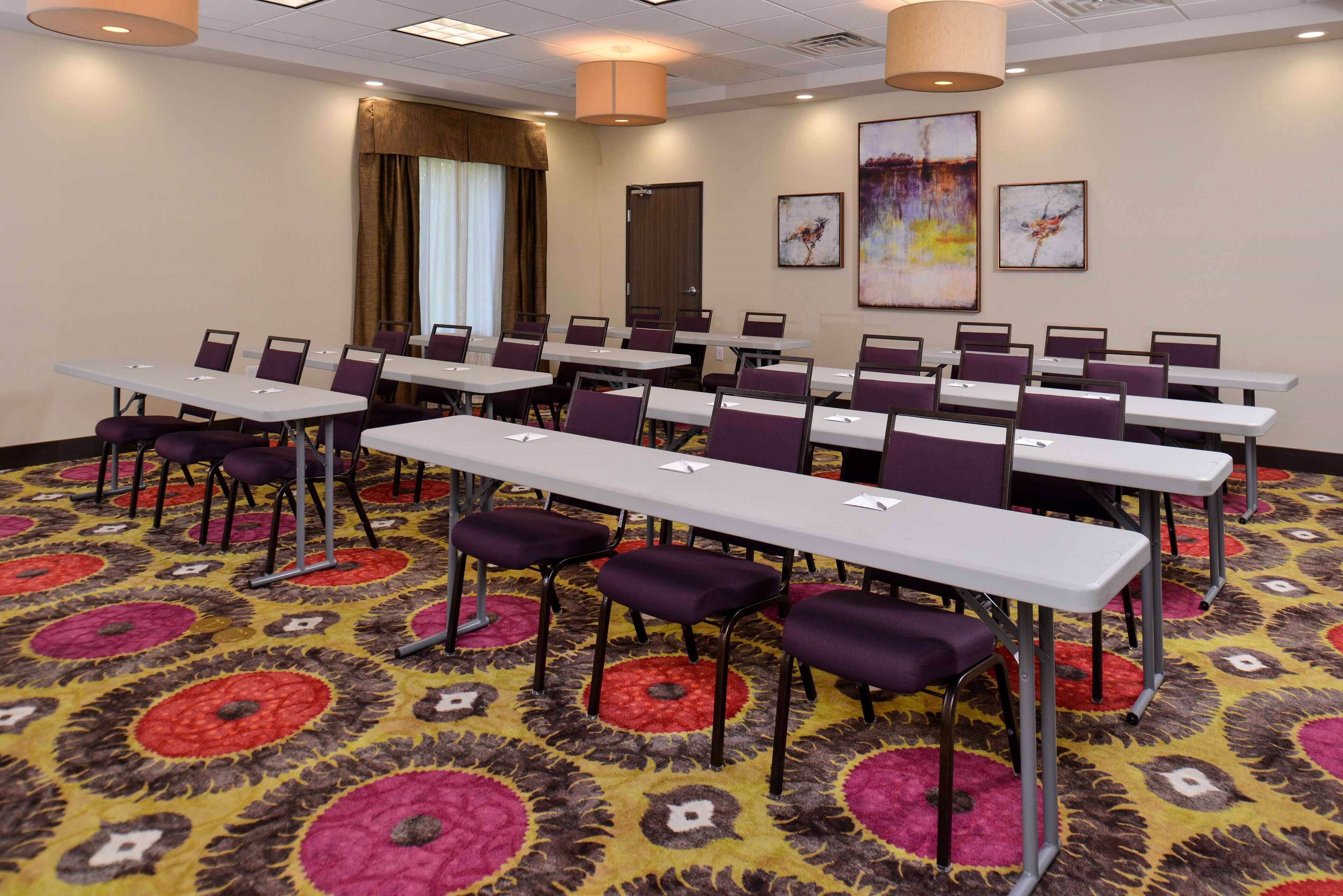 A conference room with multiple tables and chairs, a patterned carpet, and artwork on the walls.