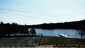 A tennis court with a view of a lake and forest. - Clark's Beach Motel (Old Forge)