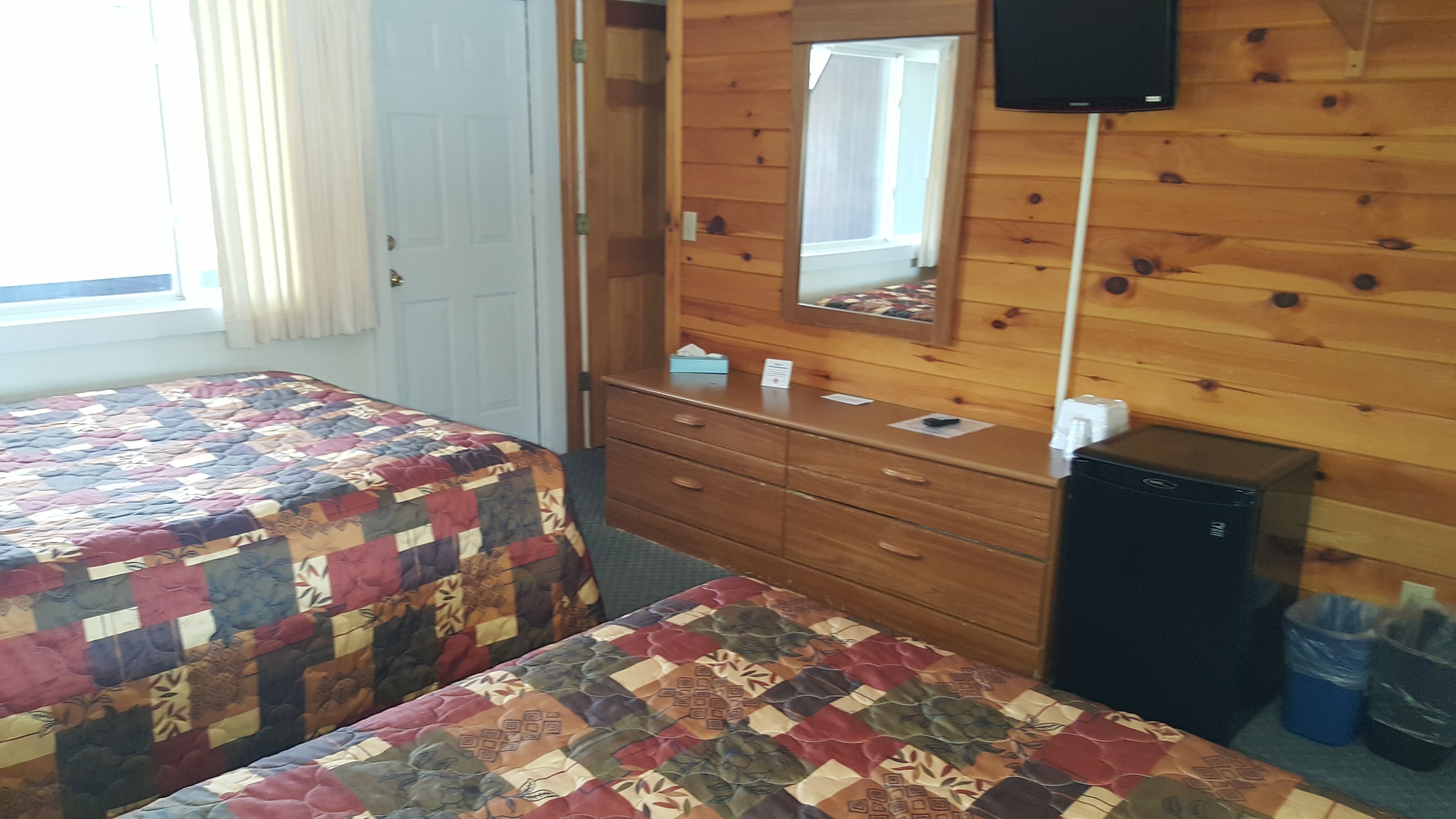 Une chambre avec deux lits, une commode en bois, un miroir, une télévision et un petit appareil électroménager noir.