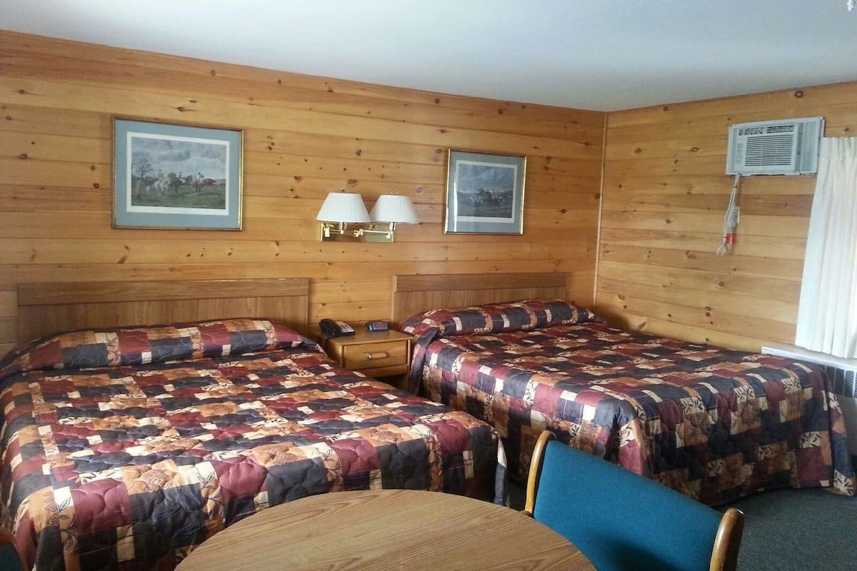 Quarto com duas camas, cabeceira de madeira, uma mesa e duas luminárias fixadas na parede.
