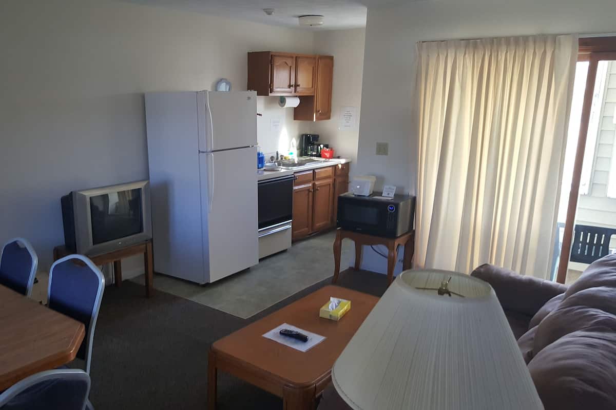 Quarto de hotel pequeno com cozinha compacta, área de jantar com mesa e cadeiras, televisão e janela com cortinas.