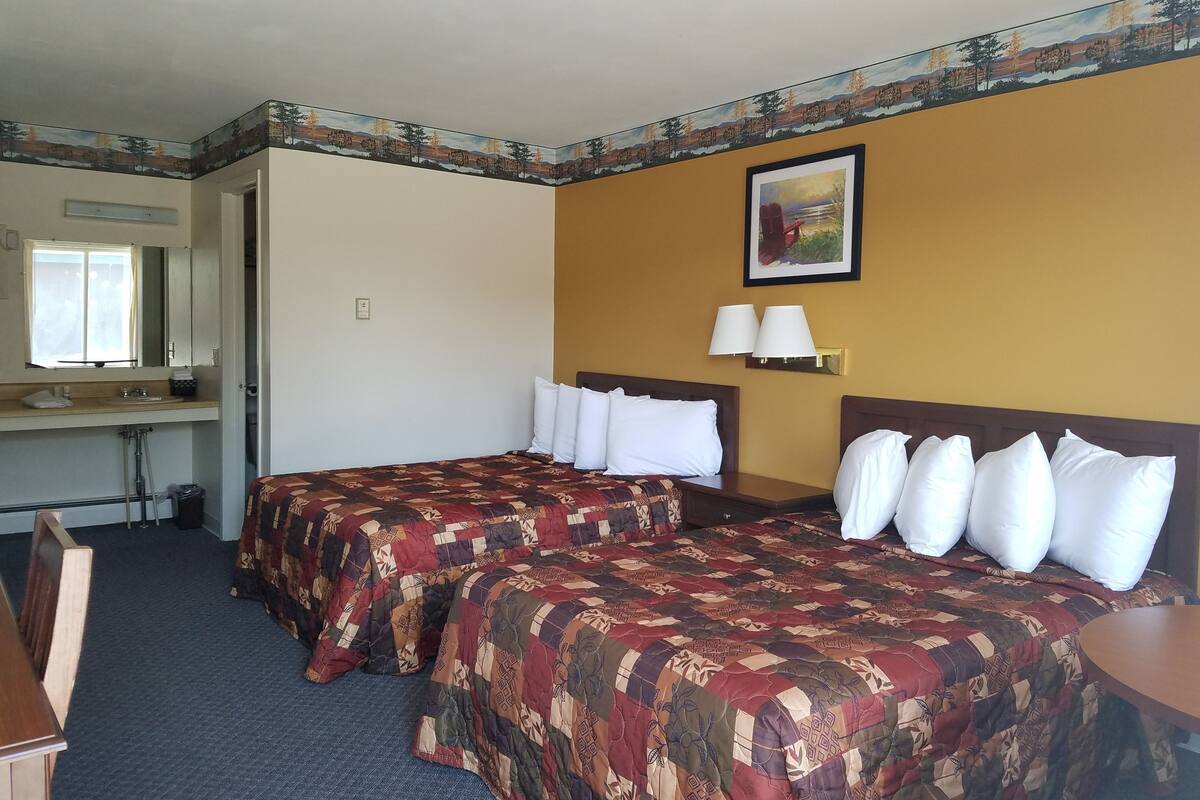 Quarto de hotel com duas camas, uma escrivaninha, uma cadeira, uma pia e uma janela.