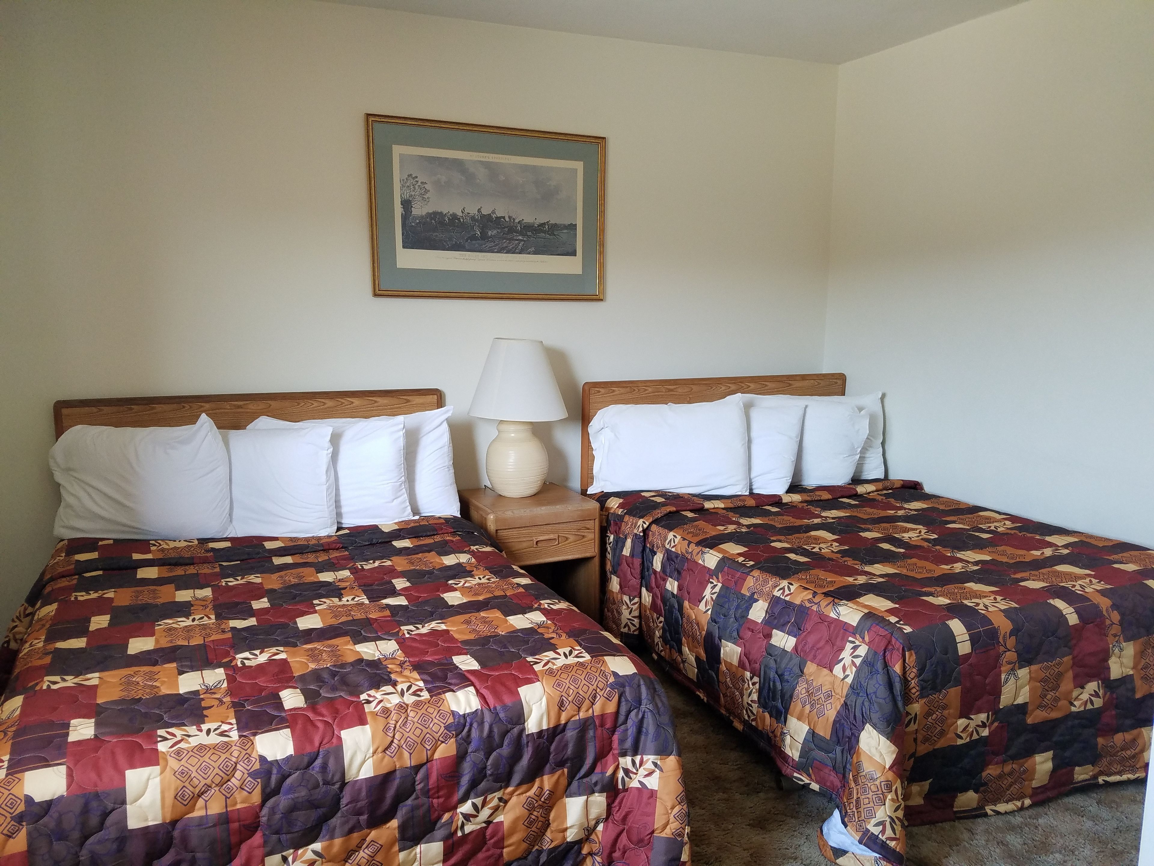 Habitación de hotel con dos camas, cada una con colcha estampada, lámpara de noche y un cuadro en la pared.