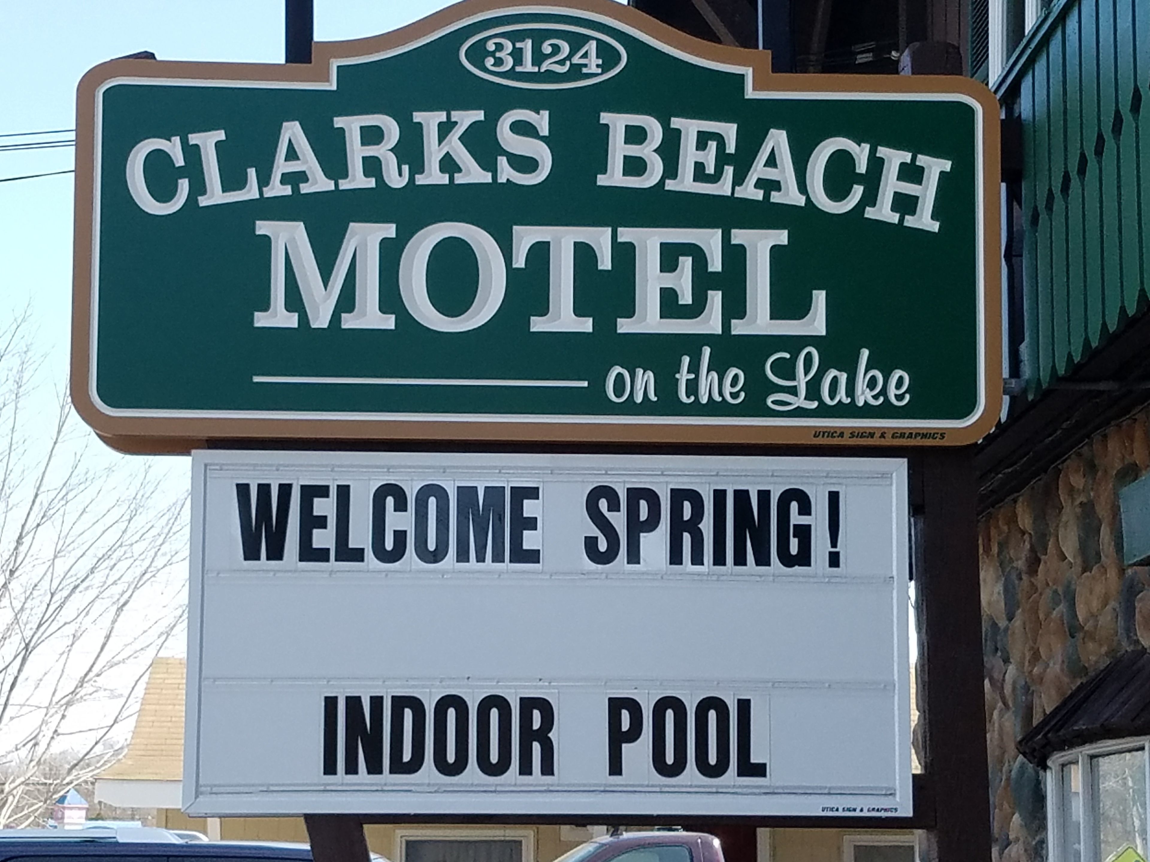 Letrero de motel que dice 'CLARKS BEACH MOTEL en el Lago' y un cartel de bienvenida para la primavera con piscina interior.