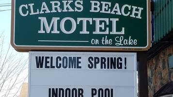 Letrero de motel que dice 'CLARKS BEACH MOTEL en el Lago' y un cartel de bienvenida para la primavera con piscina interior.