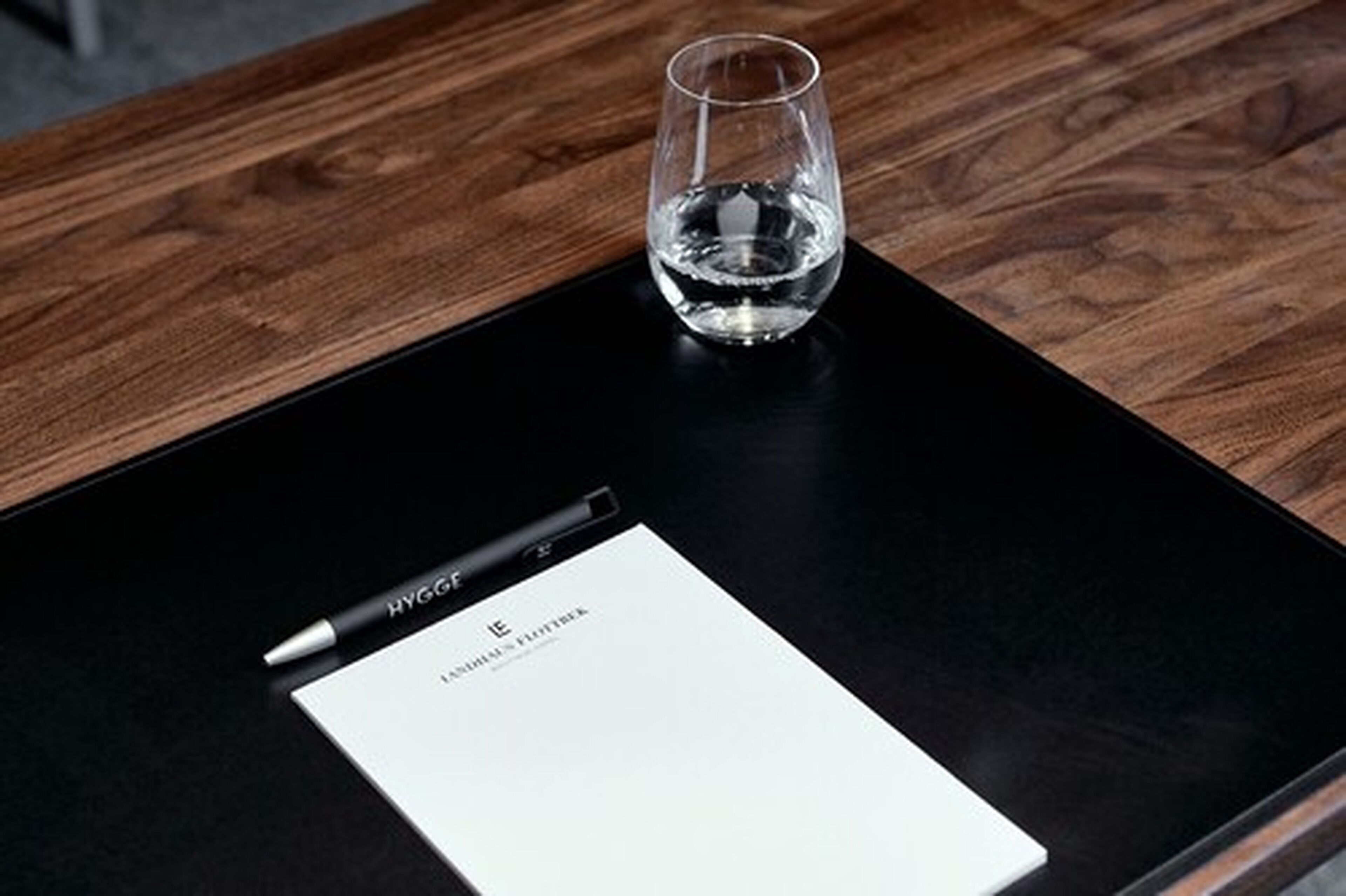 A black tray with a pen and a glass of water on a wooden table.