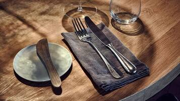 A wooden table with a folded napkin, a fork, a knife, and a glass.