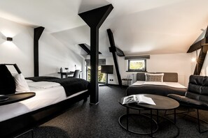 A modern hotel room with a loft-style ceiling, a bed, a sofa, a reading chair, and a small table. - Landhaus Flottbek (Hamburg)