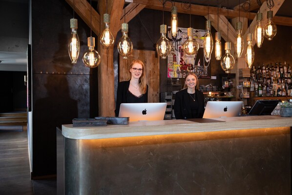 A reception area with two staff members, wooden ceiling beams, and a bar in the background. - Landhaus Flottbek (Hamburg)