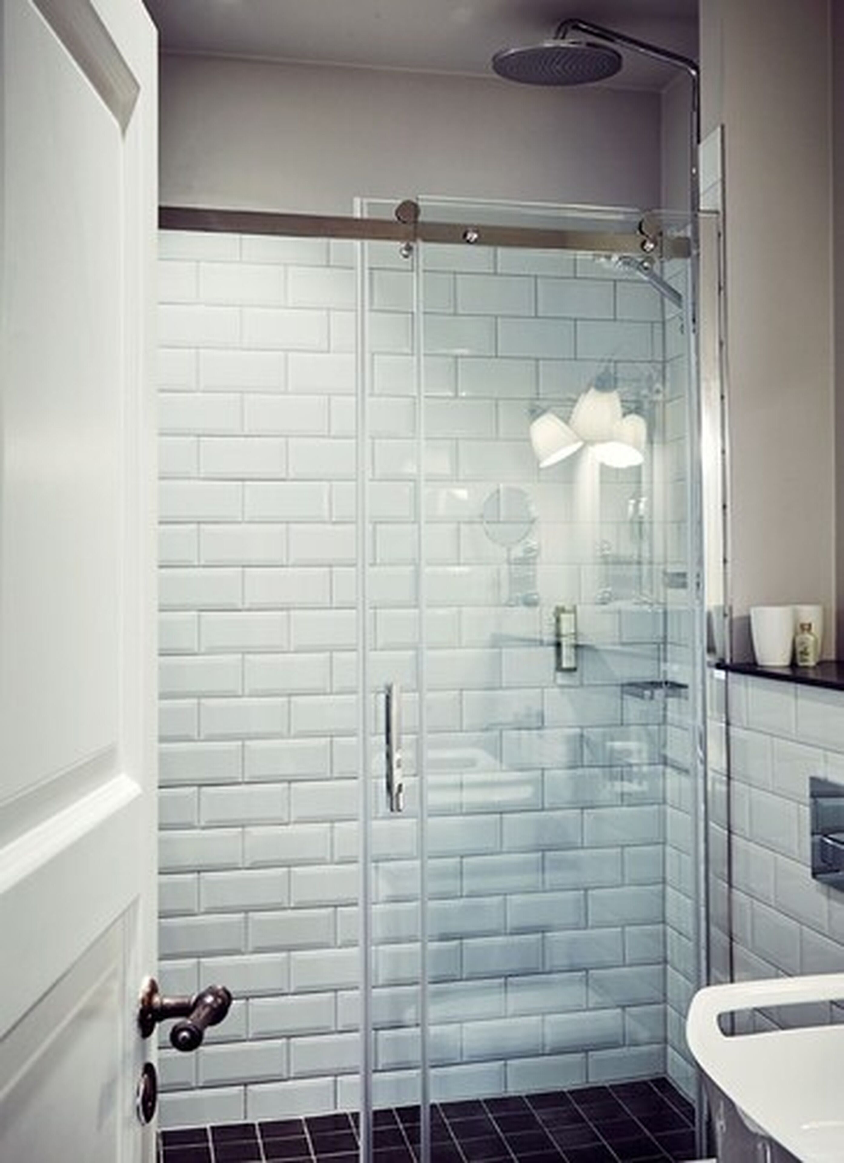 A modern bathroom with white subway tile walls, a glass shower enclosure, and a white sink.