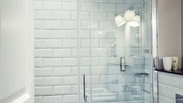 A modern bathroom with white subway tile walls, a glass shower enclosure, and a white sink.