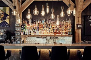 A bar with a wooden interior, hanging light bulbs, and a variety of liquor bottles. - Landhaus Flottbek (Hamburg)