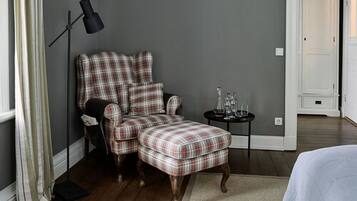 Quarto com poltrona e apoio para os pés xadrez, candeeiro de chão e pequena mesa com copos.