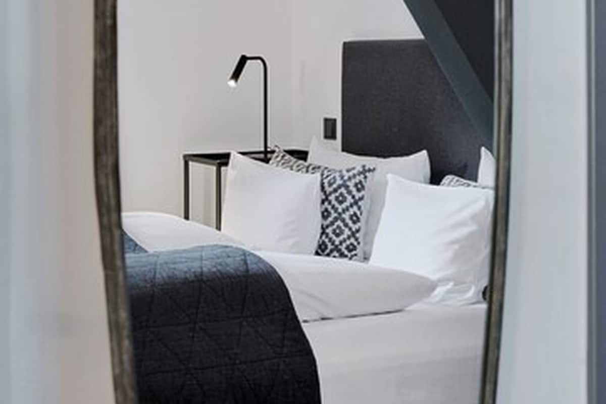 A bedroom with a bed, a bedside table, a lamp, and a mirror.