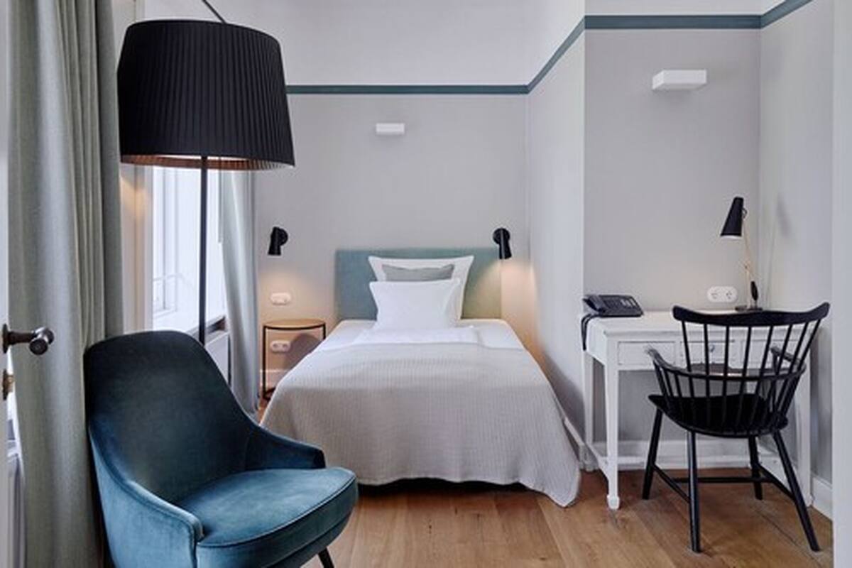 A hotel room with a bed, a desk, a chair, and a lamp.