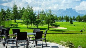 A golf course with a view of mountains, outdoor seating, and a clear sky. - Hotel Royal (Riederalp)