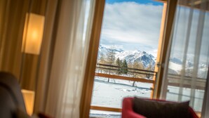 A room with a large window offering a view of snow-covered mountains and a railway track. - Hotel Royal (Riederalp)