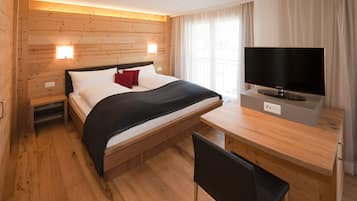 Habitació d'hotel amb paret de fusta, un llit amb almoades blanques i vermelles, un edredó negre, un televisor sobre un suport de fusta i un escriptori de fusta amb una cadira.