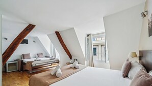 A modern hotel room with a large bed, a desk, and a chair. There is a window providing natural light and a view of the city. - Hôtel Mazagran (Paris)