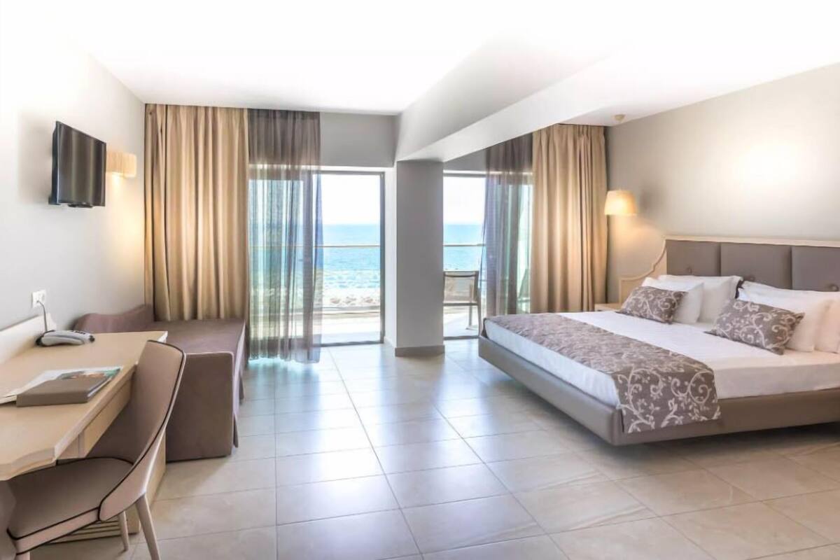A hotel room with a bed, a desk, and a view of the sea.