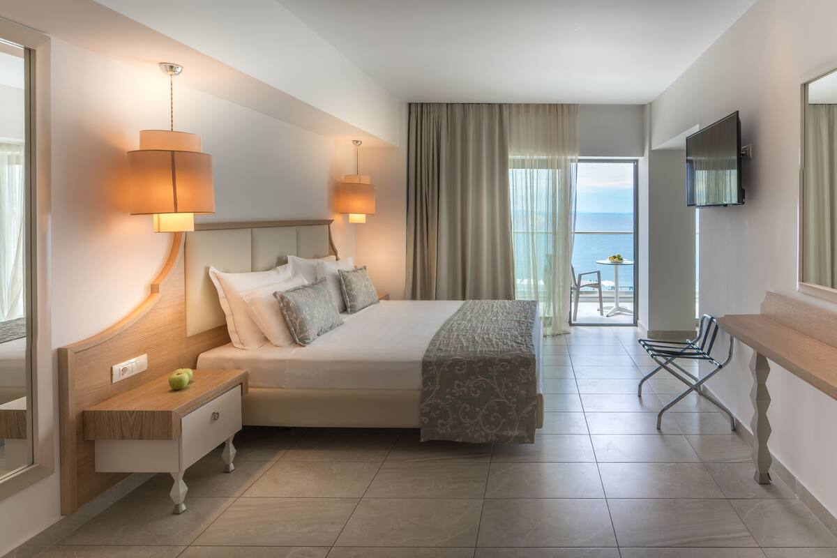 A hotel room with a bed, bedside lamps, a desk, a chair, and a TV.