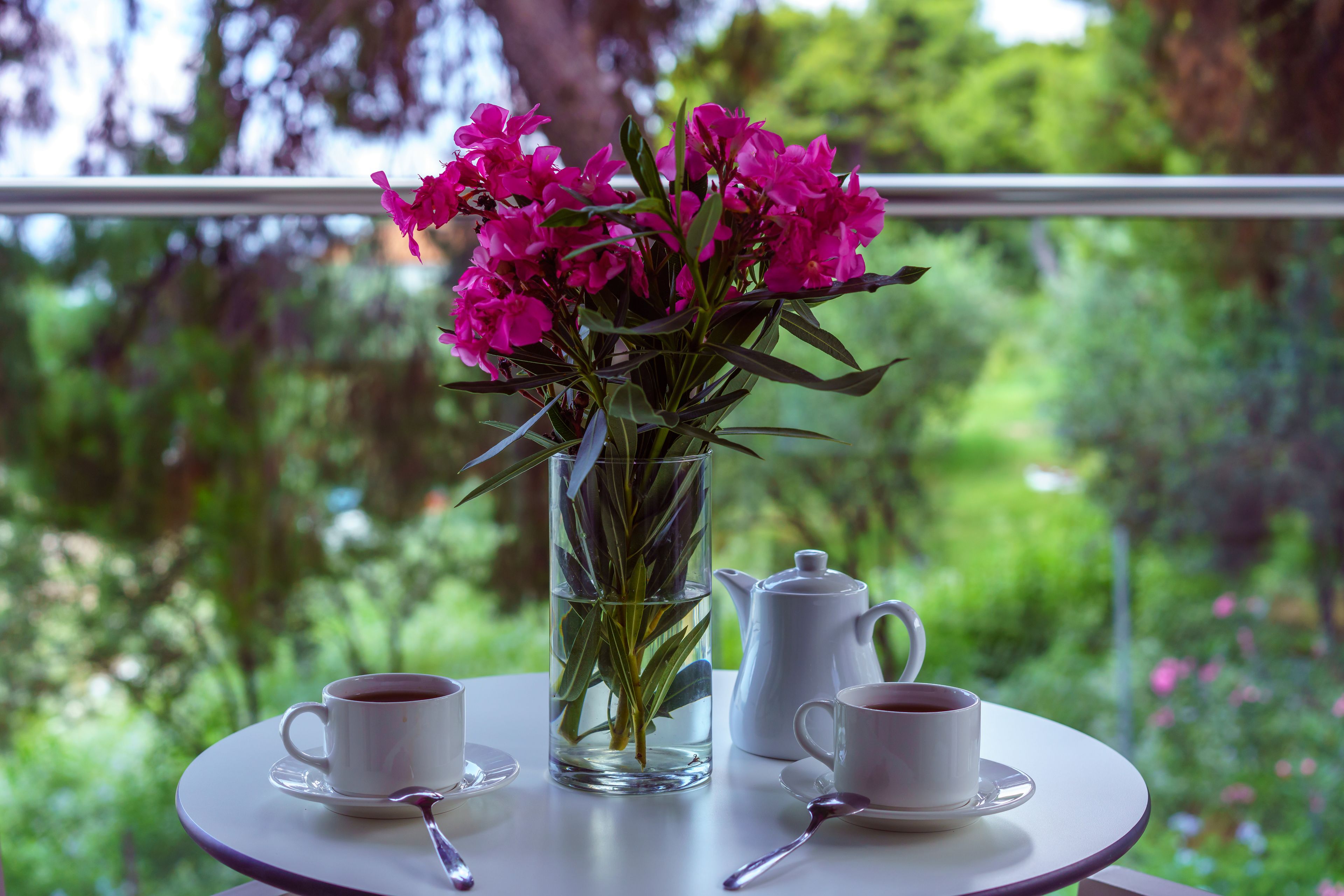 Une table avec deux tasses à café blanches, un vase transparent contenant des fleurs roses et une théière blanche.