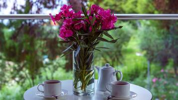 Une table avec deux tasses à café blanches, un vase transparent contenant des fleurs roses et une théière blanche.