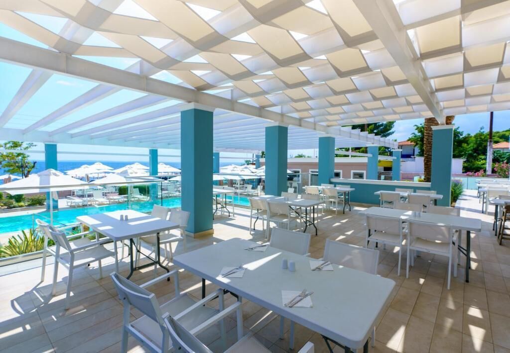 An outdoor dining area with tables and chairs, a pool, and a view of the ocean.
