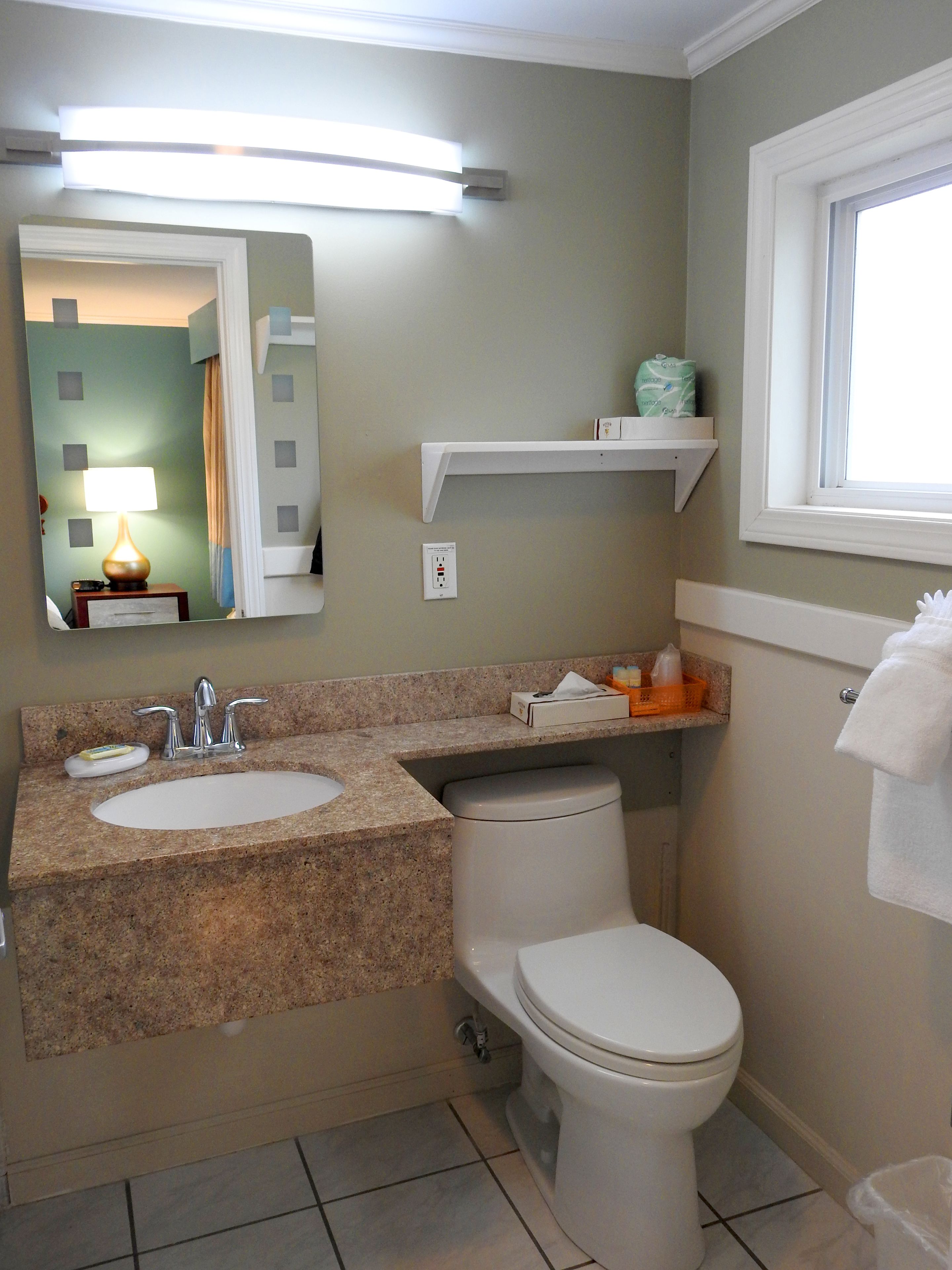 A bathroom with a granite countertop sink, a mirror, a toilet, and a window.