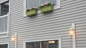 Una casa con revestimiento blanco, un balcón con barandillas blancas y dos macetas con plantas.