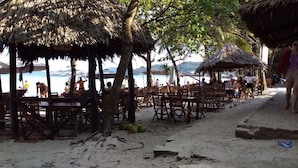 A beachside restaurant with wooden tables and chairs, a thatched roof, and a view of the sea. - Diadem Resort (Phu Quoc)