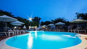 A swimming pool with lounge chairs and umbrellas, surrounded by buildings and trees. - Diadem Resort (Phu Quoc)