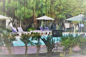 A pool area with lounge chairs and umbrellas, surrounded by lush greenery. - Diadem Resort (Phu Quoc)