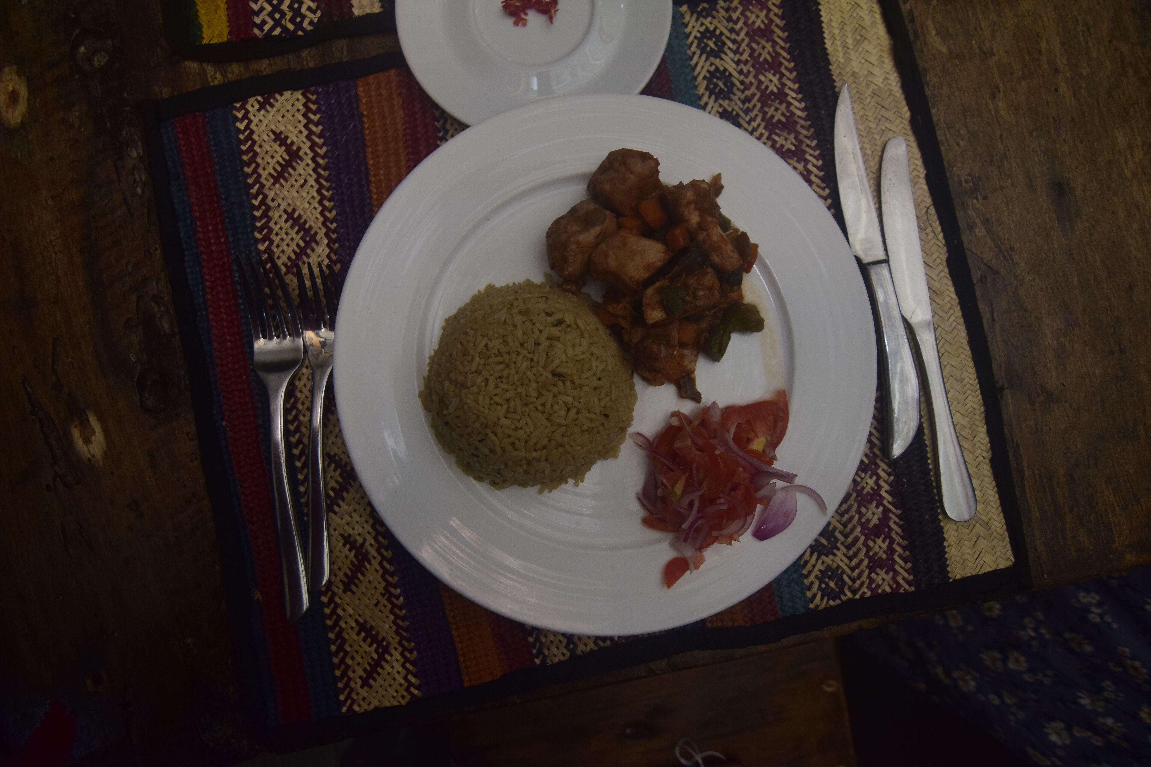 A plate with rice, meat, and vegetables on a patterned tablecloth.