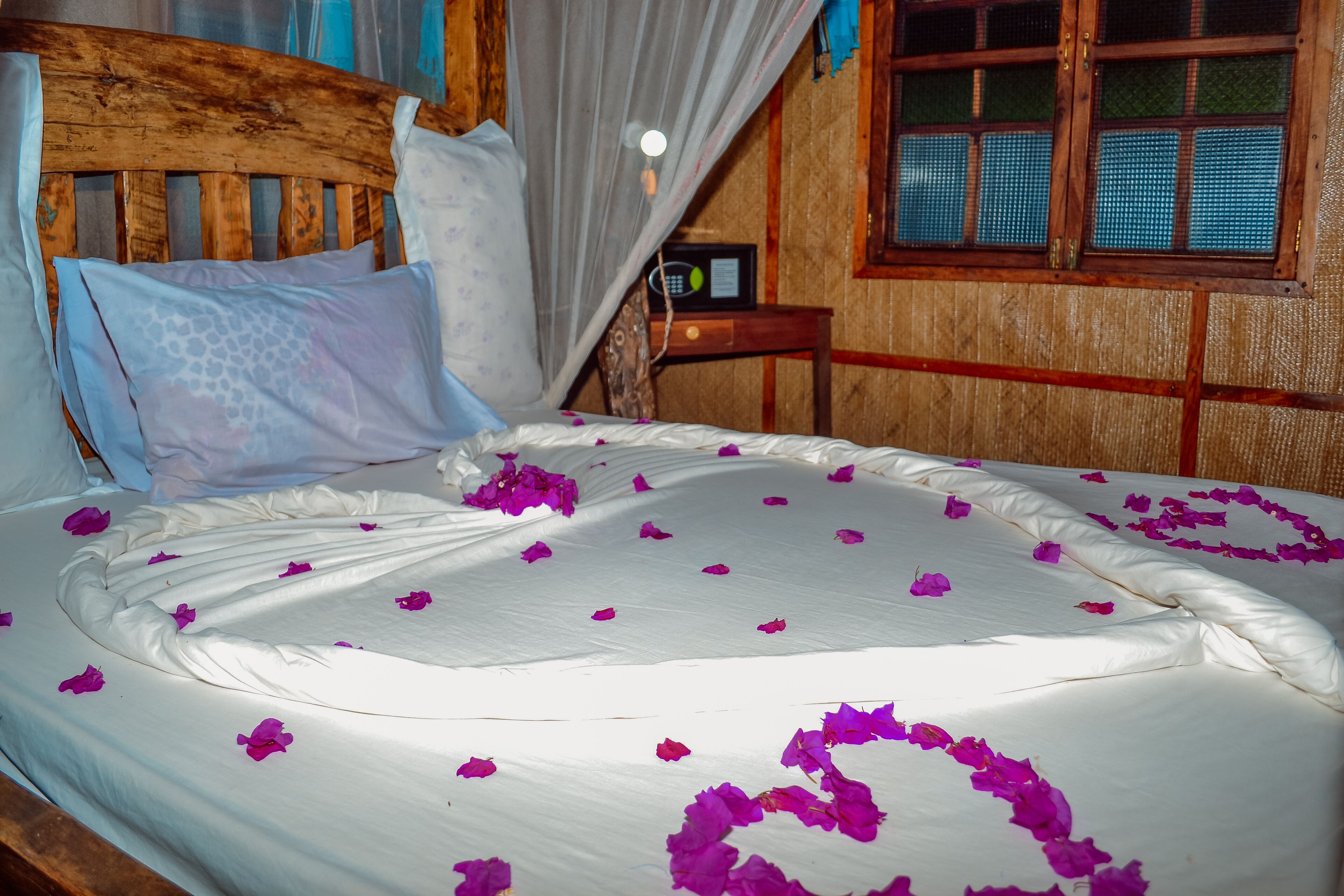 A bed with white linens, a wooden headboard, and a window with a wooden frame.
