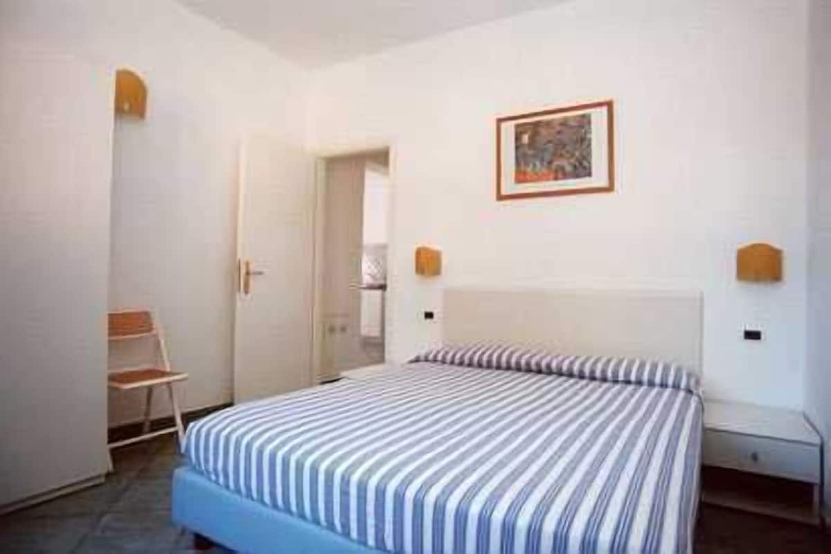 Quarto com cama, cadeira, porta e quadro na parede.