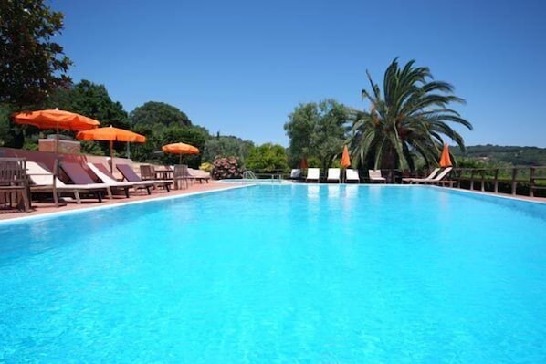 A clear blue pool with lounge chairs and orange umbrellas, surrounded by greenery.