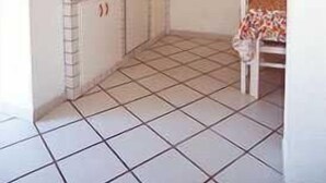 Una cocina compacta con piso de cerámica, horno empotrado y un pequeño comedor con una silla.