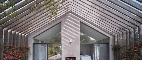 Un edificio moderno con terraza de madera, chimenea y grandes puertas de vidrio.