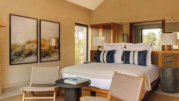 A bedroom with a large bed, two chairs, a small table, and artwork on the walls.