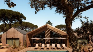 Un edificio de madera con piscina, sillas de descanso y sombrillas.