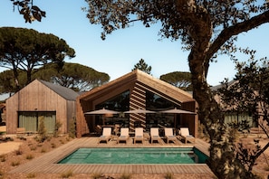 A wooden building with a pool, lounge chairs, and umbrellas.
