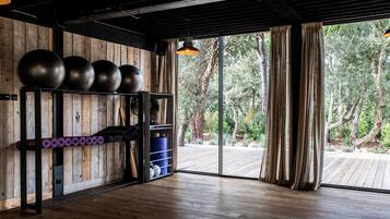 Ein Fitnessraum mit Trainingsgeräten, Holzwänden und einem großen Fenster mit Blick auf Bäume.