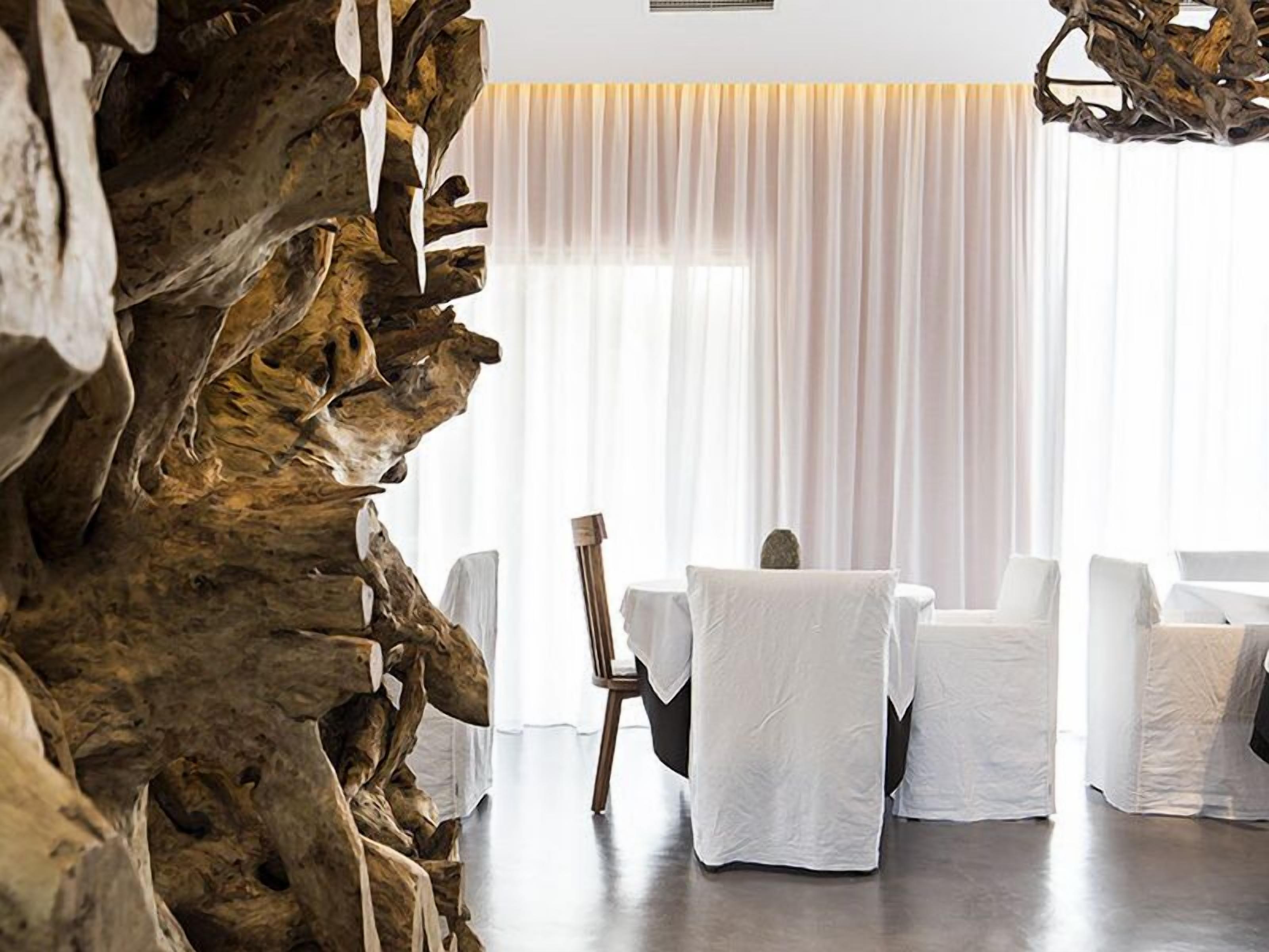 A modern room with a large wooden sculpture, white curtains, and a table with chairs.