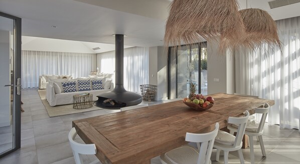 A modern living room with a large wooden dining table, white chairs, and a black fireplace. - Sublime Comporta (Grandola)