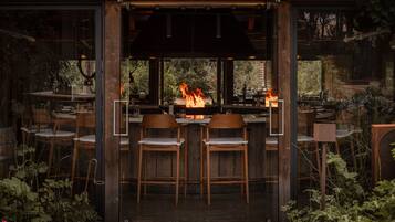 Zona de bar con chimenea, sillas de madera y vistas a través de amplios ventanales.