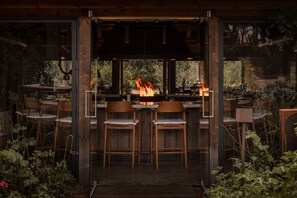 Zona de bar con chimenea, sillas de madera y vistas a través de amplios ventanales.
